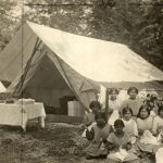 Girls sitting doing needlework in front of tent at Elizabeth Long Memorial Home summer camp.
