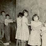 Eight children standing at chalkboard, turning to face camera