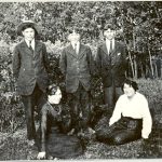 Five youth in rad, three standing, two sitting on grass