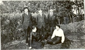 Five youth in rad, three standing, two sitting on grass