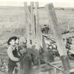 Children cutting lumber, pile of lumber in background