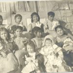 Ten young children holding dolls sitting on steps