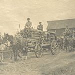 Youth on two horse drawn carts holding lumber
