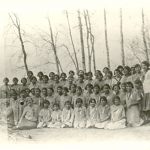 Portrait of children and staff posed in three rows with trees behind them