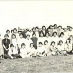 Large group of children seated and standing on a lawn.
