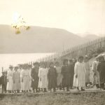 Children lined up on row wearing hats, harbour in background