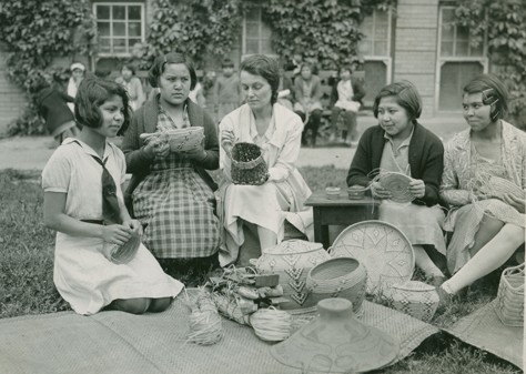 Youth sitting outside on school grounds with baskets in front of them.
