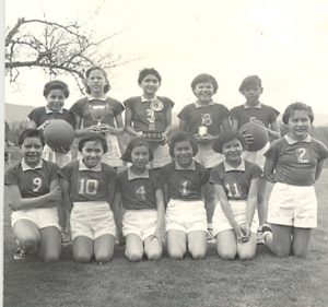 Youth in soccer uniforms, seated and standing with trophies and basketballs., outdoors.