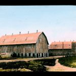 Two barns with road along side them, image hand coloured