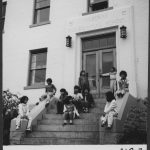 Group of children sitting on the front steps, front door with Alberni Residential School engraved overtop.