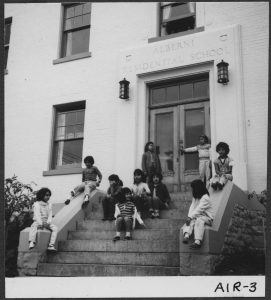 Group of children sitting on the front steps, front door with Alberni Residential School engraved overtop.