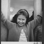 Child smiling with arms up in the air, door in the background.