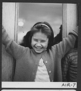 Child smiling with arms up in the air, door in the background.