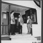 Three men standing on a porch having a conversation.