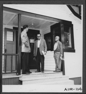 Three men standing on a porch having a conversation.