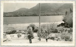 View from out the door of Ahousaht Residential School, showing two individuals, the grounds and the river.