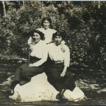 Three youth sitting on a large boulder with forest behind them