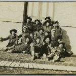 Group of children sitting on grass outside of building.