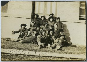 Group of children sitting on grass outside of building.