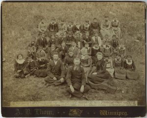Large group seated on grass, three staff members at the front (John McDougall at centre), with youth behind.