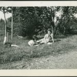 Two children laying in grass reading books by the roadside