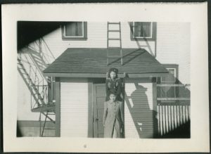 Two youth, one in front of the ladder, one standing on the ladder which is leaning on the Port Simpson Residential School building
