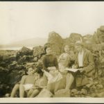Group of children with staff sitting on rocks at the beach and reading from books