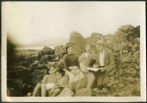 Group of children with staff sitting on rocks at the beach and reading from books