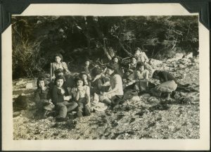 Group of children sitting on the rocky beach eating and drinking from mugs