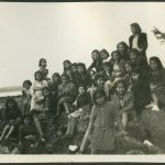 Large group of children and youth sitting and standing on boulders at the beach