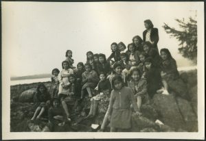 Large group of children and youth sitting and standing on boulders at the beach