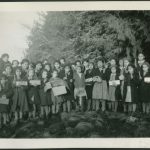 Large group of children with one staff member on the beach, they are holding candles, boxes, and other kinds of containers