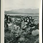Group of younger children sitting with a staff member on rocks at the beach, mountains in the background
