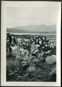 Group of younger children sitting with a staff member on rocks at the beach, mountains in the background