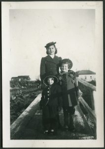 Youth with two smaller children posed together on a boardwalk with buildings behind them