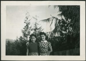 Two youth, one with arm around the other, standing in front of trees