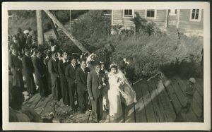 Couples in formal wedding attire paired in a line on boardwalk