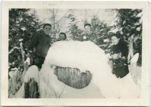 Children and staff in winter gear behind wooden structure making snowballs