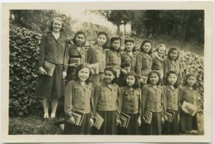 Staff member and youth standing in front of a hedge wearing uniforms and holding bundles of books