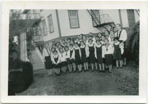 Children and group leaders in Canadian Girls in Training uniforms standing in front of Port Simpson Residential School building