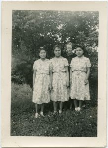 Three youth in identical dresses standing with a staff member in front of trees