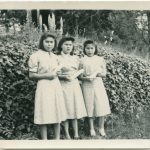 Three youth holding rolled diplomas standing in front of a tall hedge