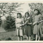 Three youth holding rolled diplomas in field with small trees
