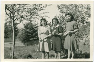 Three youth holding rolled diplomas in field with small trees