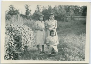 Three youth holding rolled diplomas standing next to tall hedge, one youth is kneeling