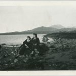 Two youth sitting on boulders on the beach at low tide