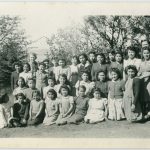 Group portrait of children, youth, and staff in field with small trees