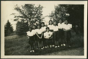 Group of youth with softball, bat, and trophy, posed in a field