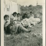 Youth sitting by clothesline of drying laundry mending garments