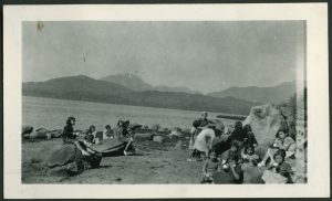 Children and staff on the beach, eating and drinking from mugs, children are sitting on big boulders